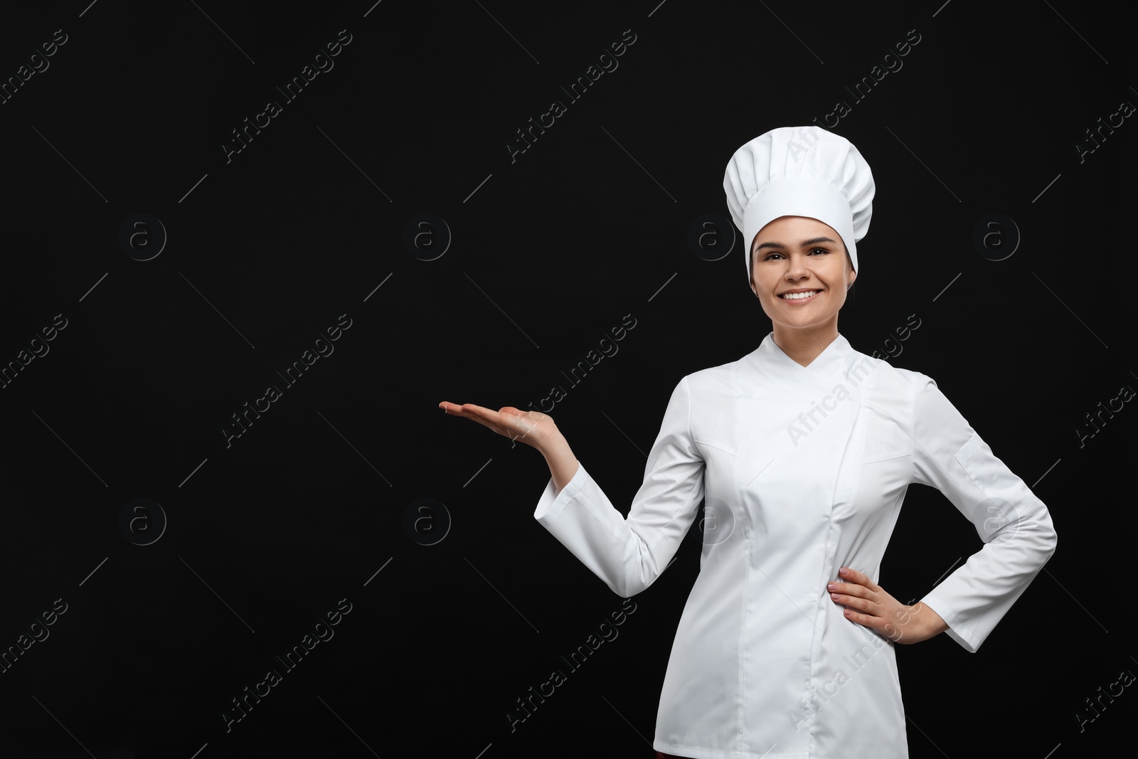 Photo of Happy female chef pointing at something on black background. Space for text