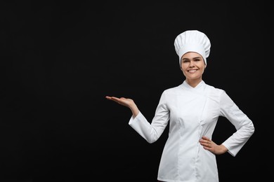 Happy female chef pointing at something on black background. Space for text