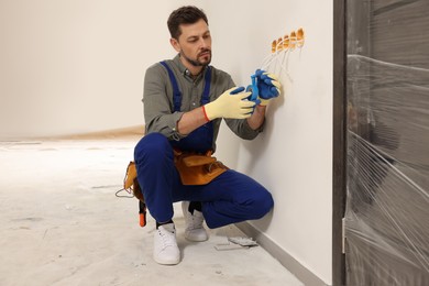 Photo of Electrician in uniform with insulating tape repairing power socket indoors