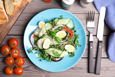 Salad with fresh organic microgreen in plate on wooden table, flat lay