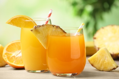Photo of Pineapple and orange juices in glasses on white table, closeup