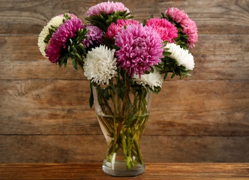Photo of Beautiful asters in vase on table against wooden background. Autumn flowers