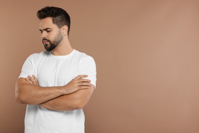 Photo of Portrait of resentful man with crossed arms on brown background. Space for text