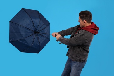 Man with umbrella caught in gust of wind on light blue background
