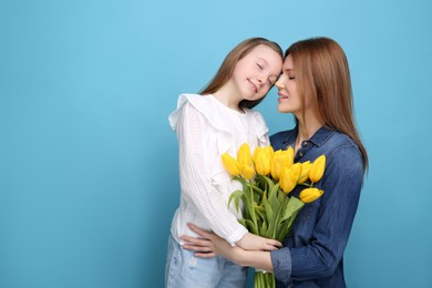 Mother and her cute daughter with bouquet of yellow tulips on light blue background