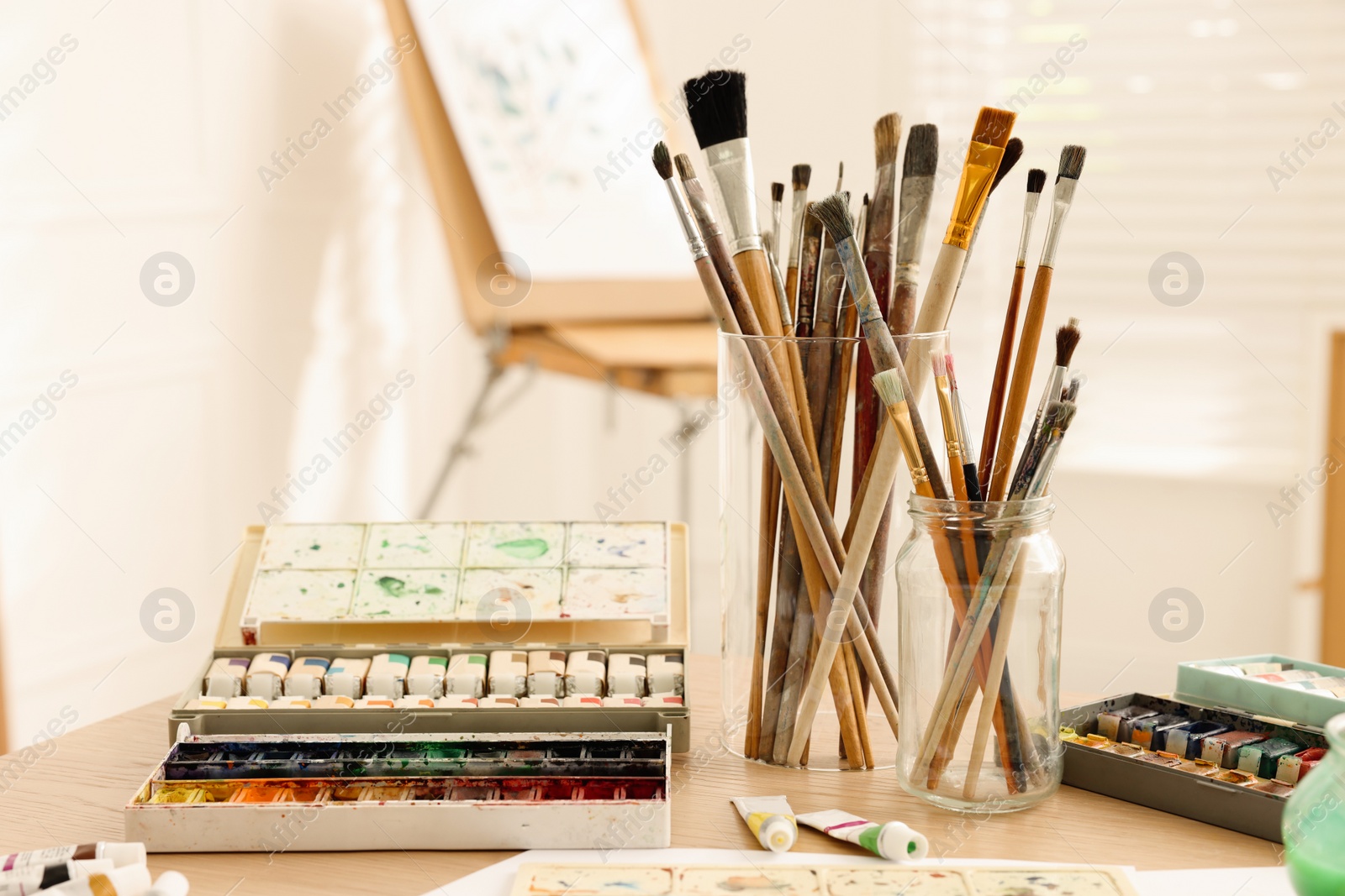 Photo of Different brushes and paints on wooden table in studio. Artist's workplace