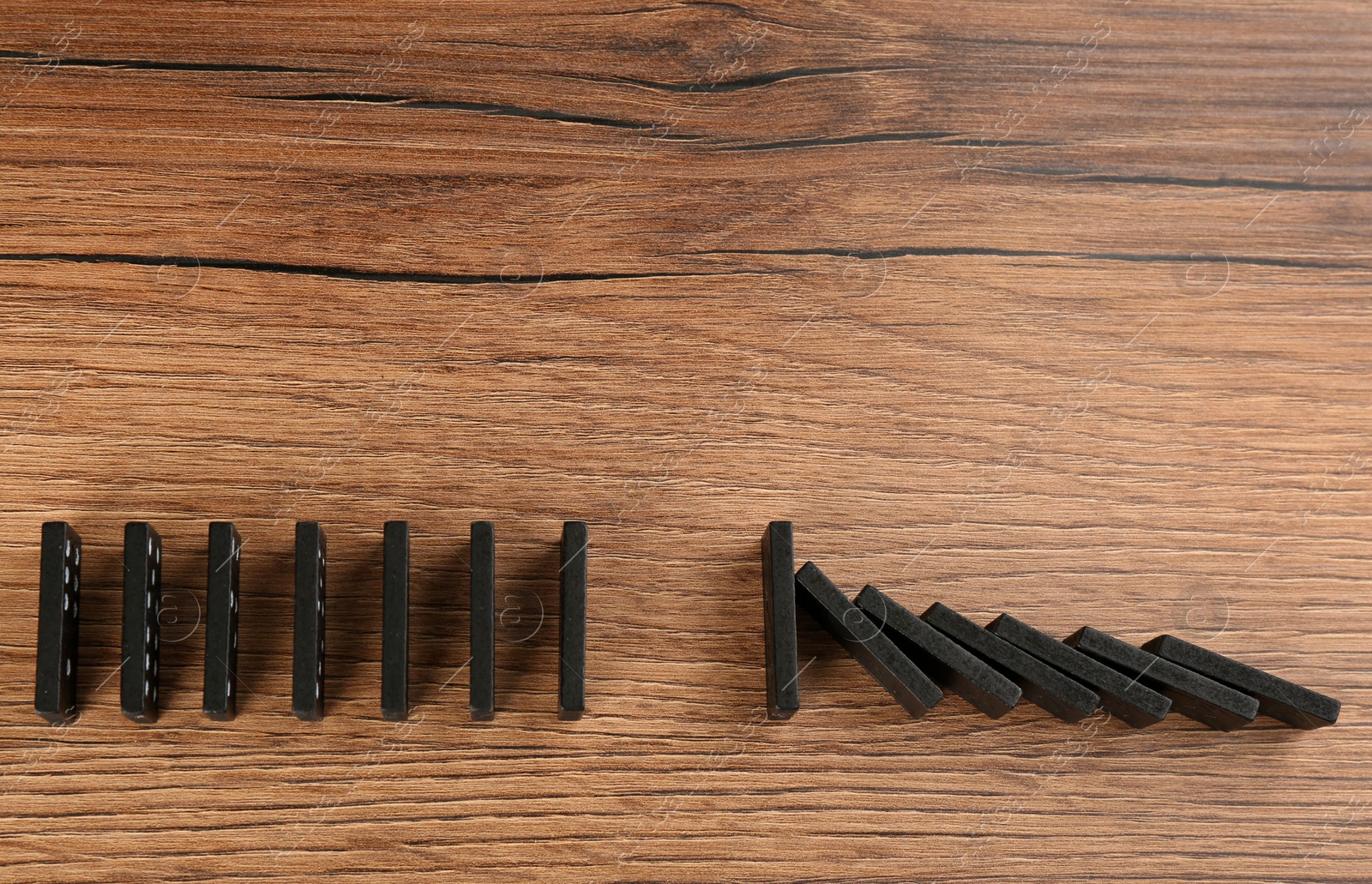 Photo of Black domino tiles on wooden background, flat lay. Space for text