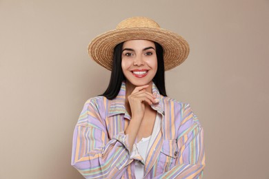 Beautiful young woman with straw hat on beige background