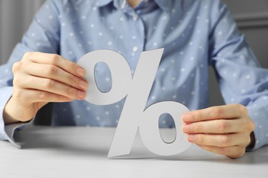 Photo of Woman holding percent sign at white wooden table, closeup