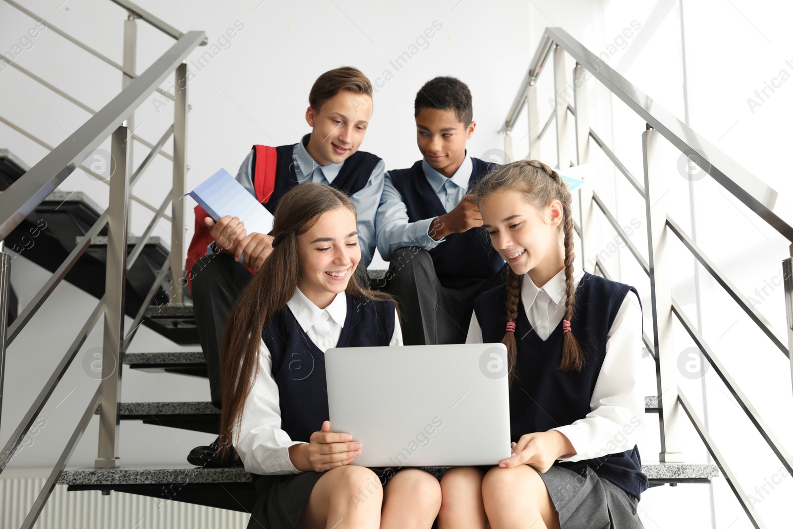 Photo of Teenage students in stylish school uniform on stairs indoors
