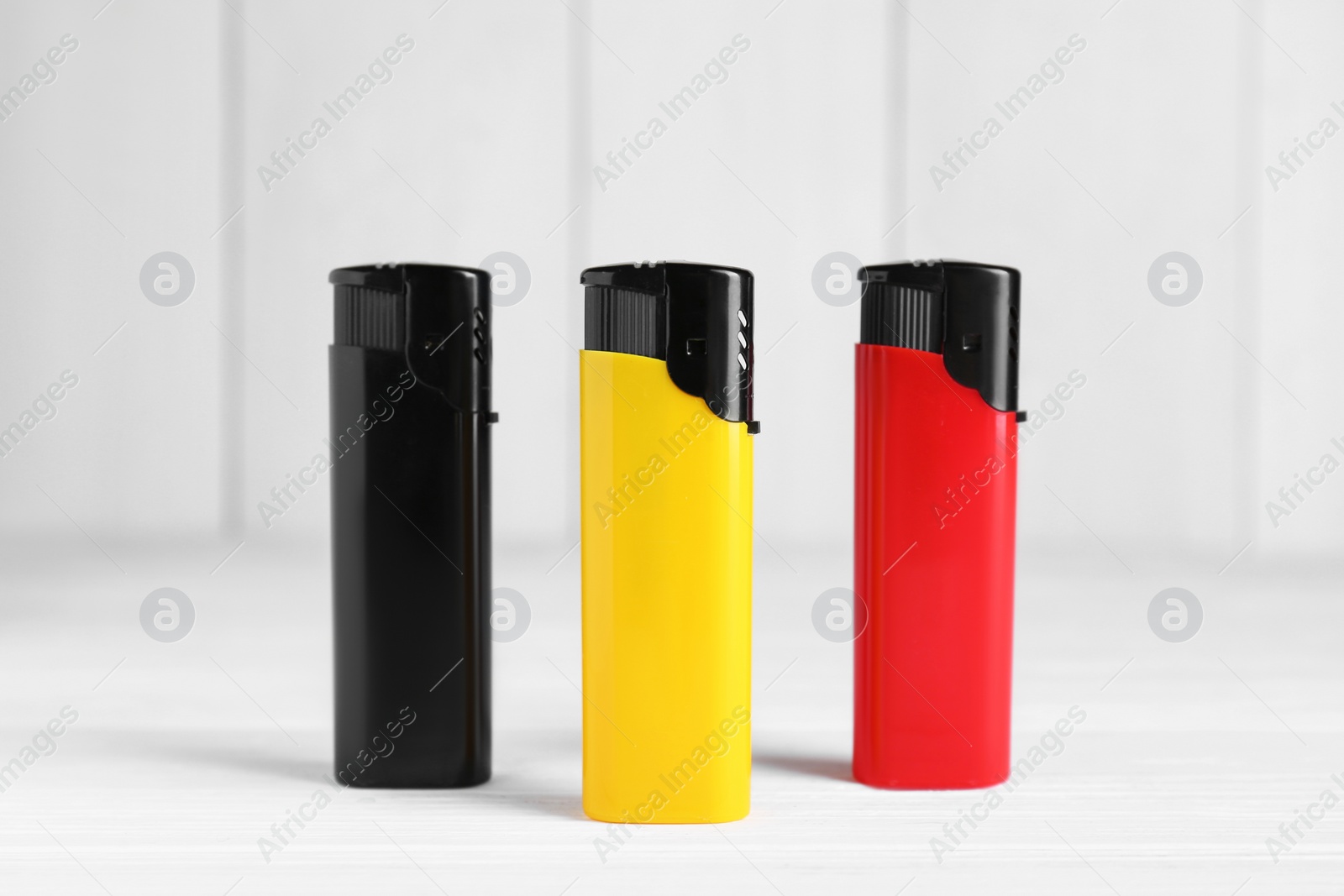 Photo of Stylish small pocket lighters on white wooden table