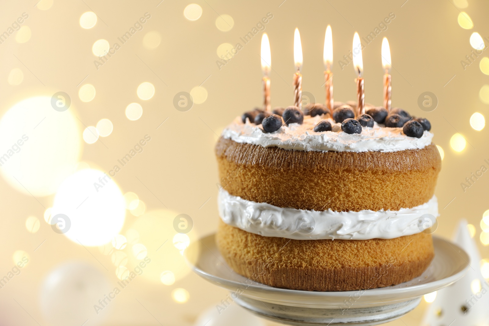 Photo of Tasty cake with burning candles on beige background against blurred lights, closeup. Space for text