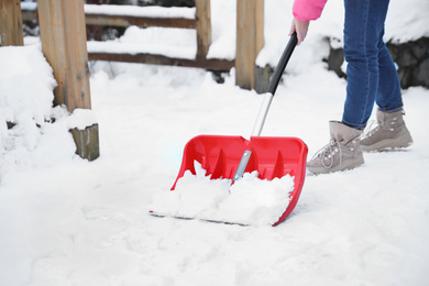 Photo of Woman cleaning snow with shovel outdoors on winter day, closeup