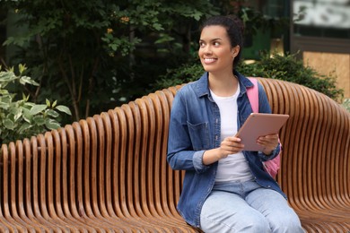 Happy student with tablet on bench outdoors, space for text