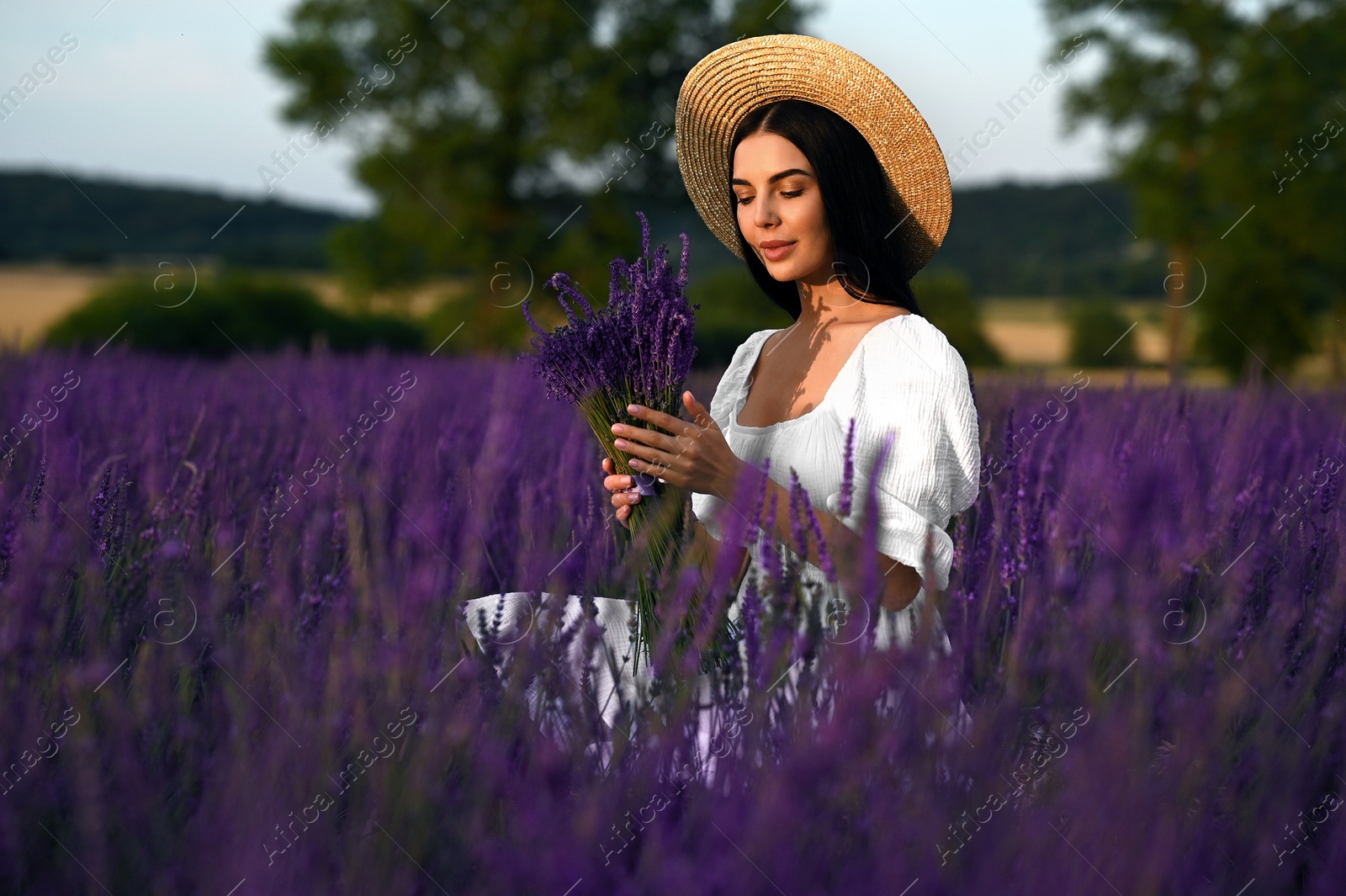 Photo of Beautiful young woman with bouquet sitting in lavender field