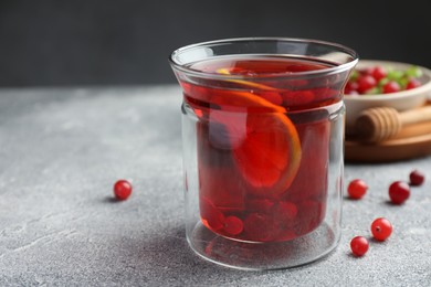 Tasty hot cranberry tea with lemon and fresh berries in glass on light grey textured table