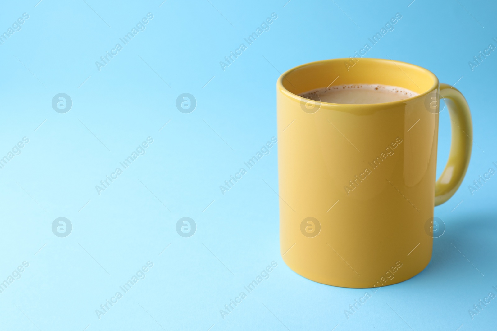 Photo of Yellow mug of freshly brewed hot coffee on light blue background, space for text