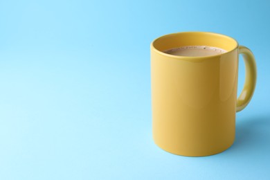 Photo of Yellow mug of freshly brewed hot coffee on light blue background, space for text