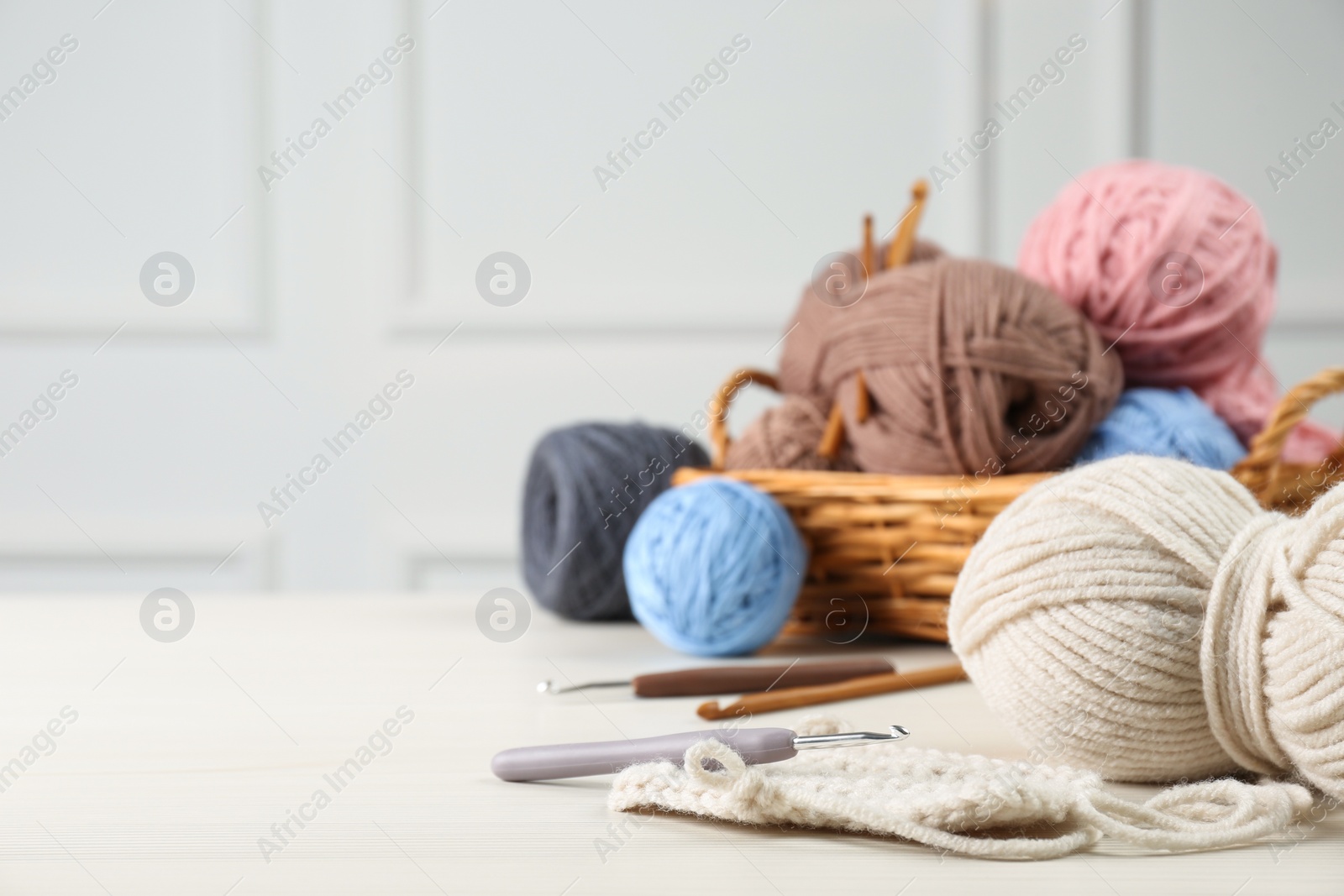 Photo of Clews of colorful knitting threads and crochet hooks on white wooden table, space for text