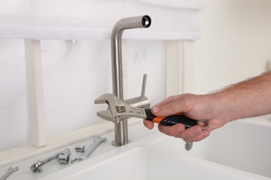 Man with wrench near sink in kitchen, closeup. Water tap installation