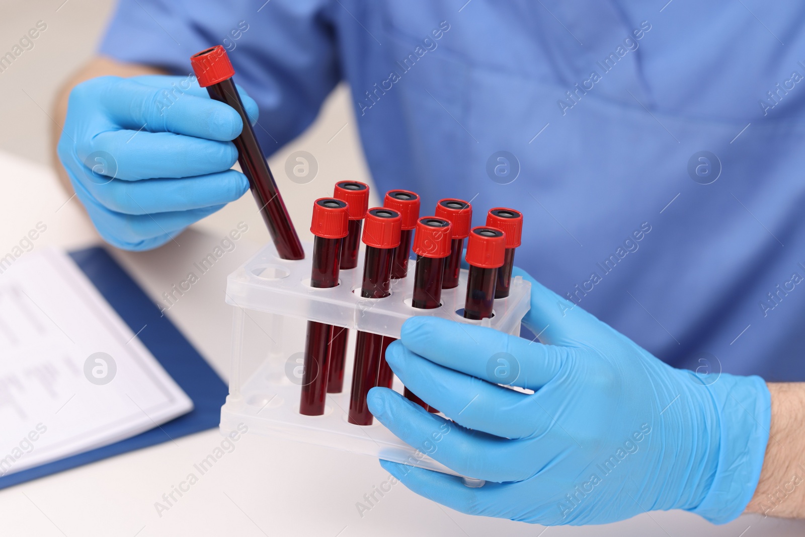 Photo of Doctor with samples of blood in test tubes at white table, closeup