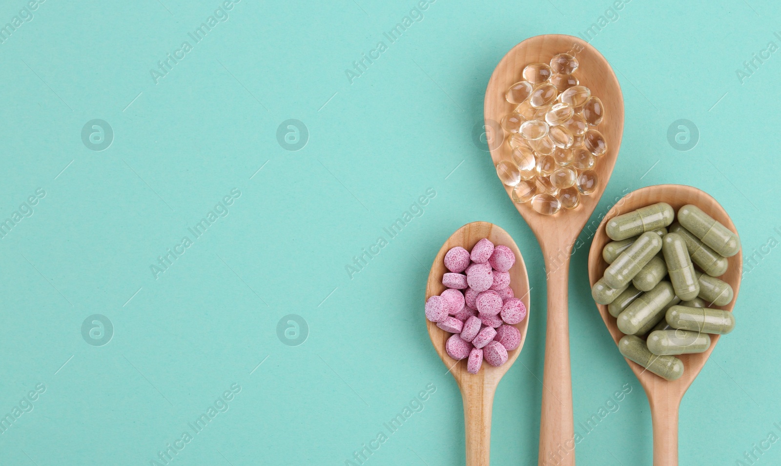 Photo of Different vitamin pills in wooden spoons on turquoise background, flat lay. Space for text