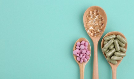 Different vitamin pills in wooden spoons on turquoise background, flat lay. Space for text