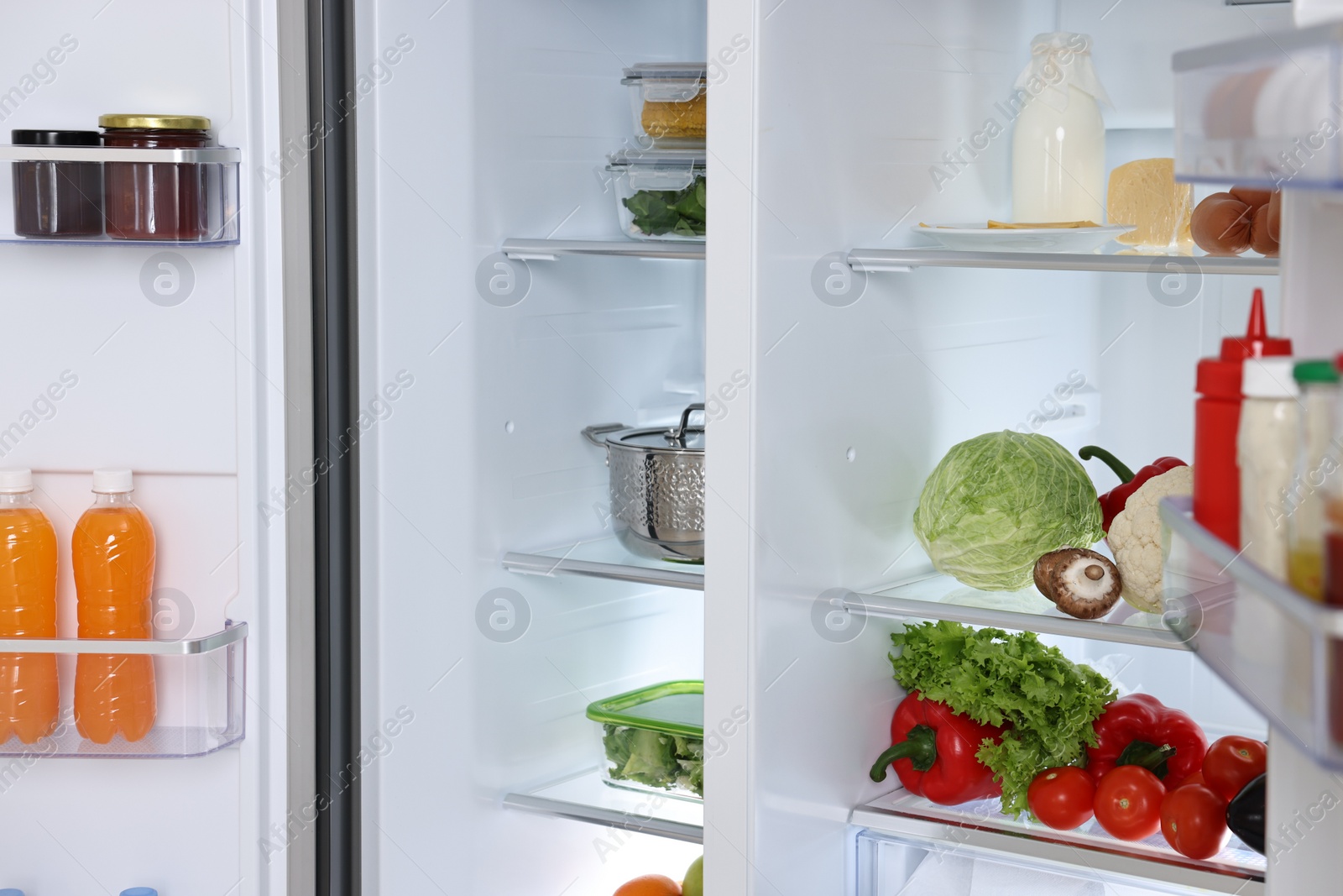 Photo of Open refrigerator full of different products indoors