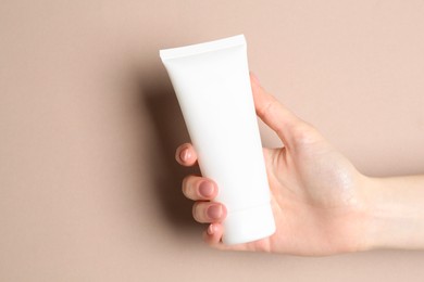 Woman with tube of cream on beige background, closeup