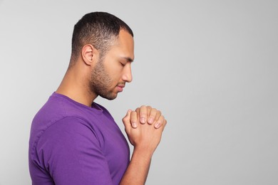 Photo of African American man with clasped hands praying to God on light grey background. Space for text