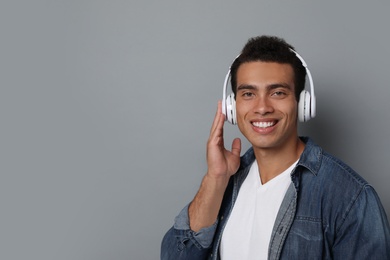 Handsome young African-American man with headphones listening to music against grey background. Space for text