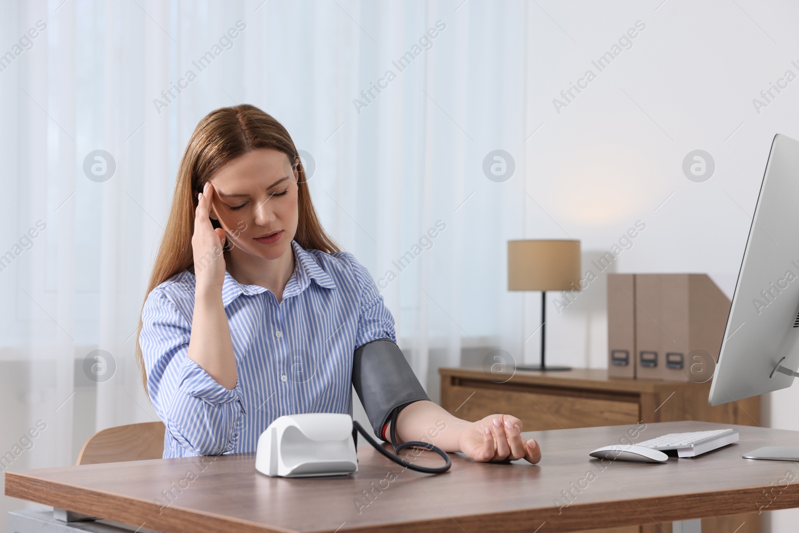 Photo of Woman suffering from headache and measuring blood pressure at wooden table in room, space for text