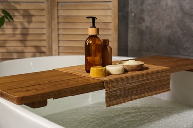 Photo of Wooden tray with spa products on bath tub in bathroom