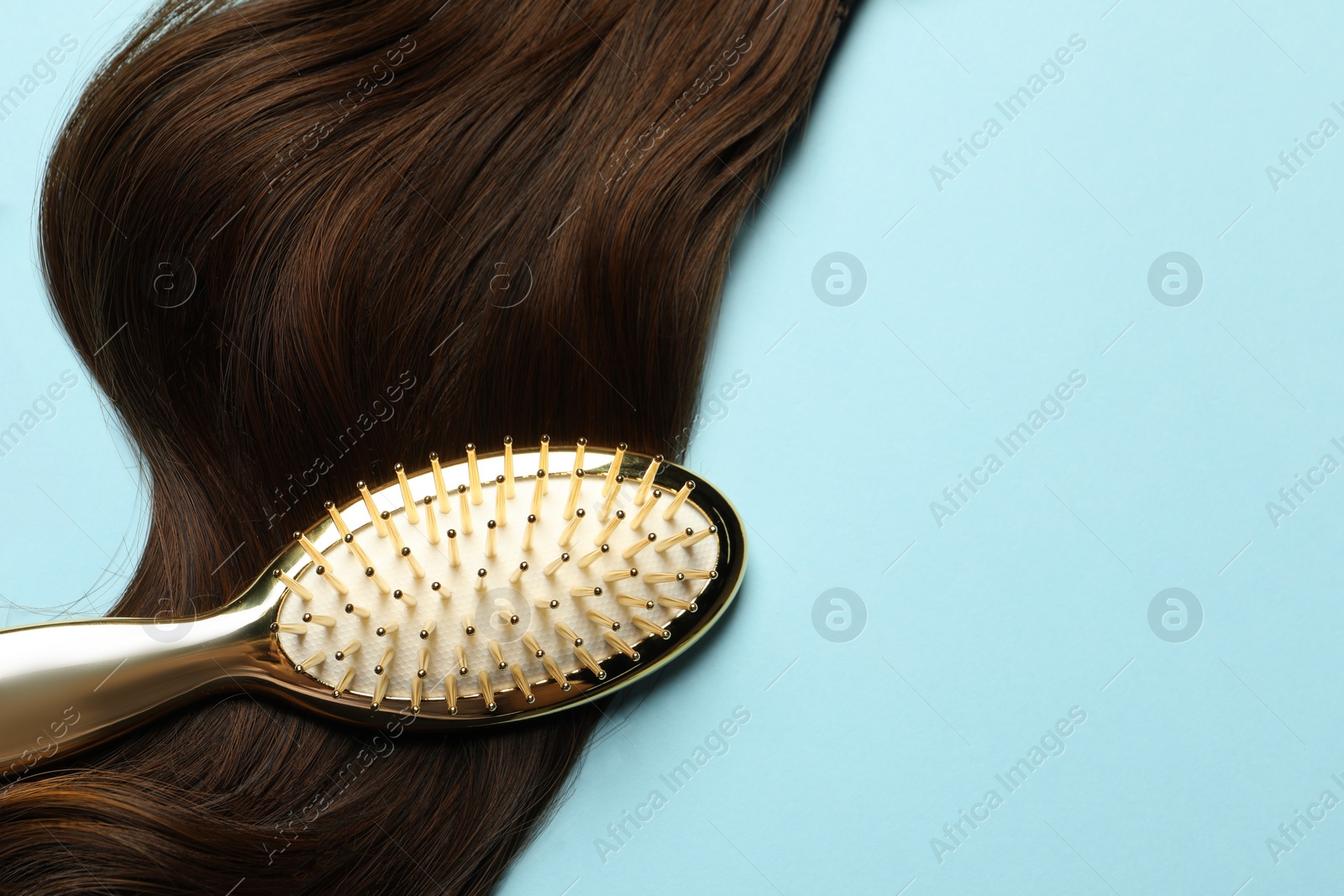 Photo of Stylish brush with brown hair strand on light blue background, top view. Space for text