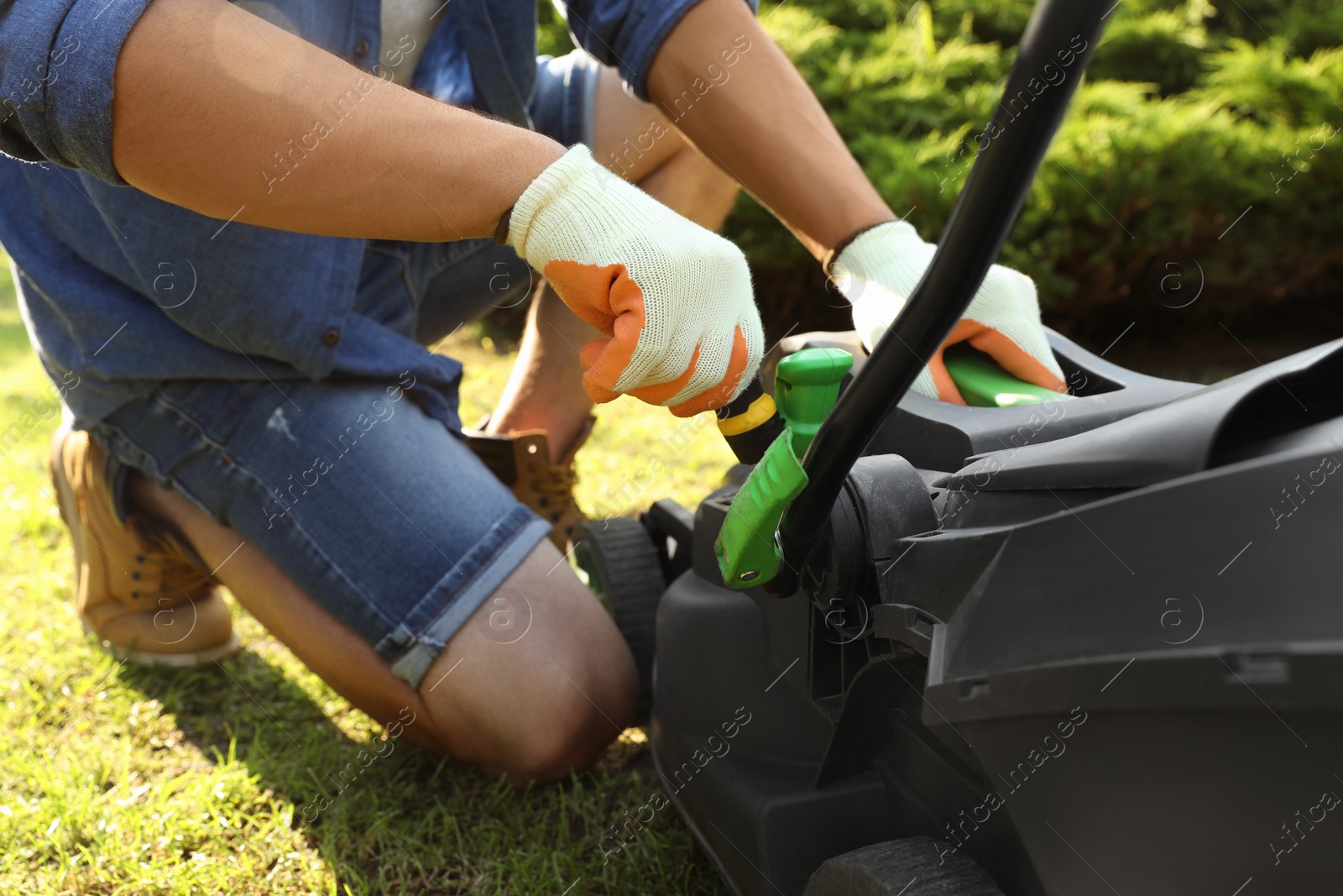 Photo of Young man with screwdriver fixing lawn mower in garden, closeup