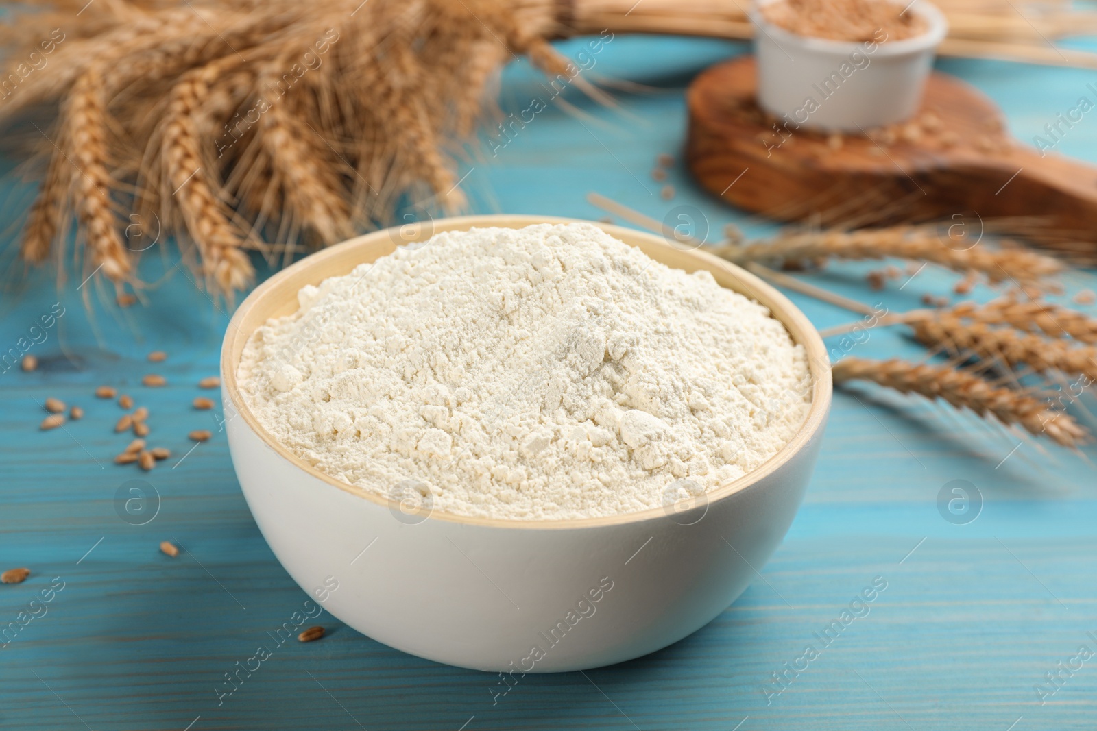 Photo of Wheat flour in bowl on light blue wooden table