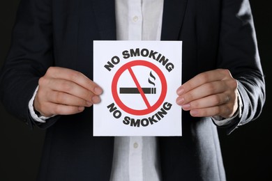 Photo of Woman holding card with no smoking sign on black background, closeup