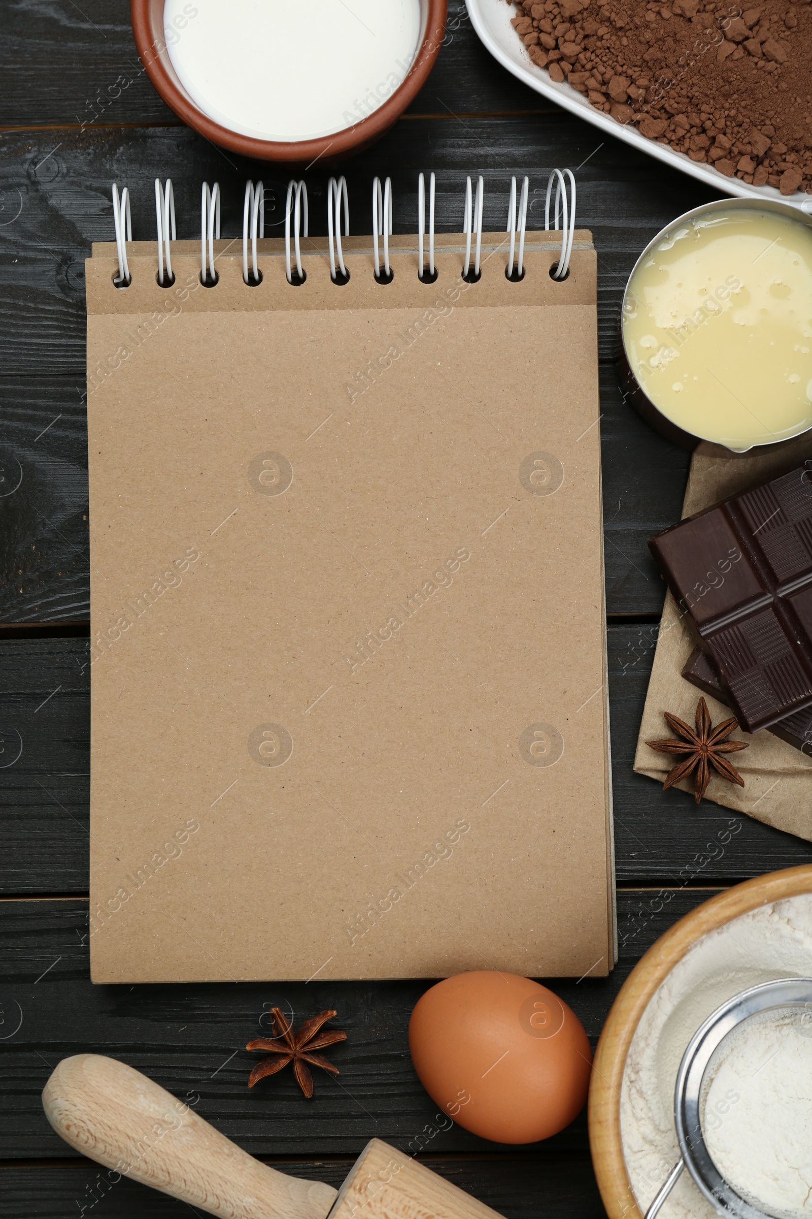 Photo of Blank recipe book and different ingredients on black wooden table, flat lay. Space for text