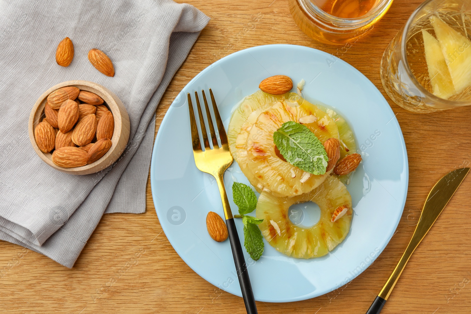 Photo of Tasty grilled pineapple slices served with mint and almonds on wooden table, flat lay