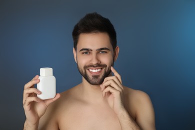 Photo of Handsome young man with beard holding post shave lotion on blue background
