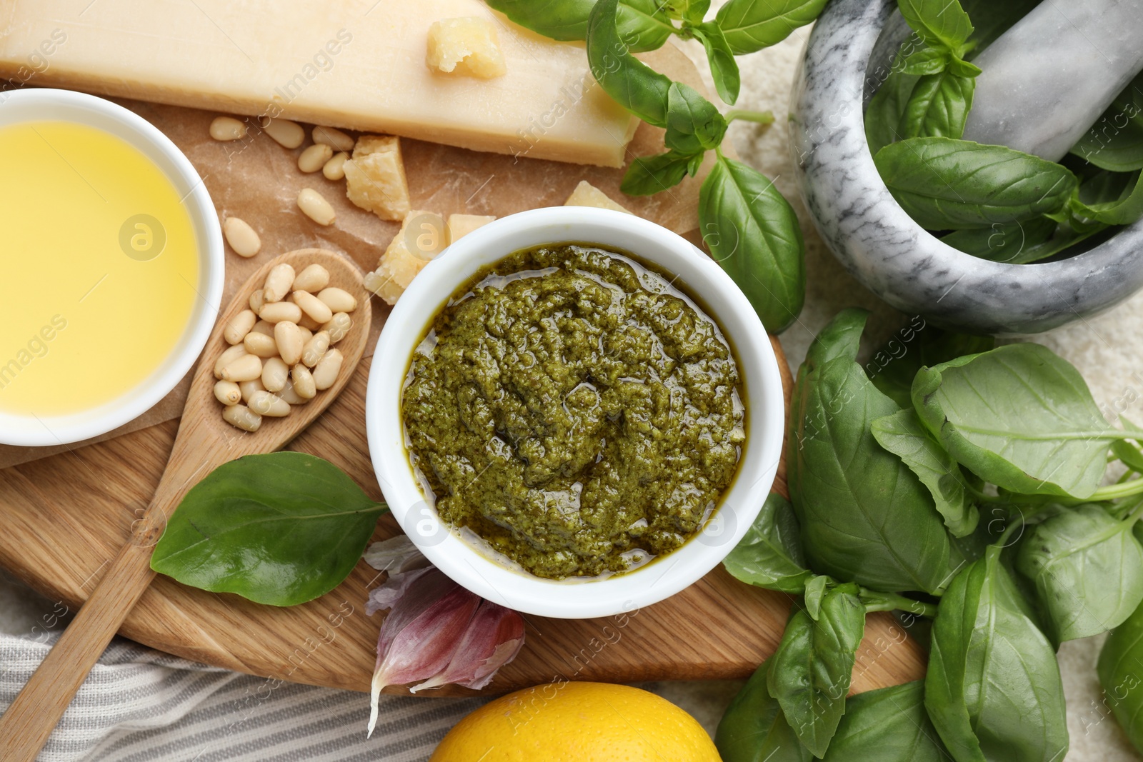 Photo of Tasty pesto sauce in bowl, basil, pine nuts, garlic, oil and cheese on table, top view