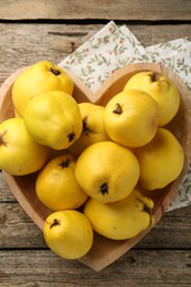 Photo of Tasty ripe quinces in heart shaped bowl on wooden table, top view
