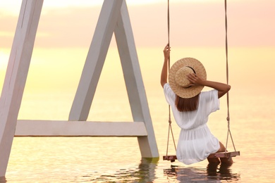 Photo of Young woman enjoying sunrise on swing over water