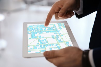 Man analyzing cadastral map on tablet indoors, closeup 