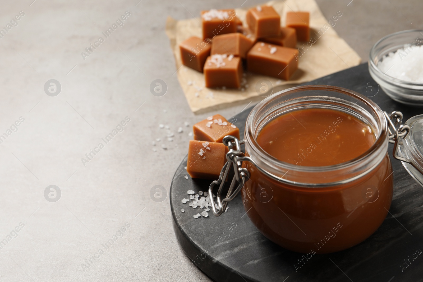 Photo of Tasty salted caramel in glass jar on grey table, space for text