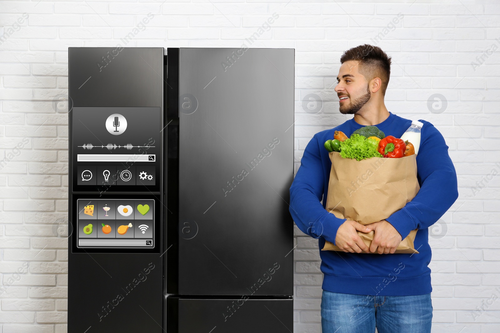 Image of Young man with bag of groceries near smart refrigerator indoors