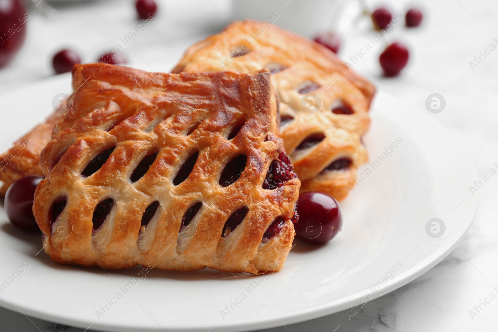 Photo of Fresh delicious puff pastry with sweet cherries served on white marble table, closeup