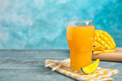 Photo of Glass of fresh mango juice and tasty fruits on wooden table. Space for text