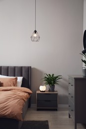 Stylish bedroom interior with comfortable bed, nightstand and green houseplant