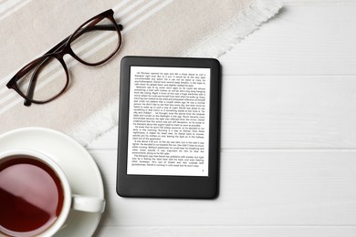 Portable e-book reader, glasses and cup of tea on white wooden table, flat lay. Space for text